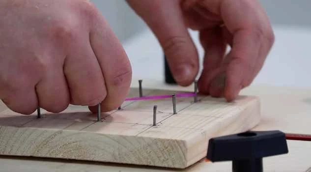 Hands stretching a band between the nails of a wooden geoboard to form a shape.