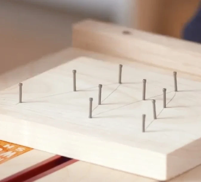 Nails placed upright around a lightly sketched design on a pine board.