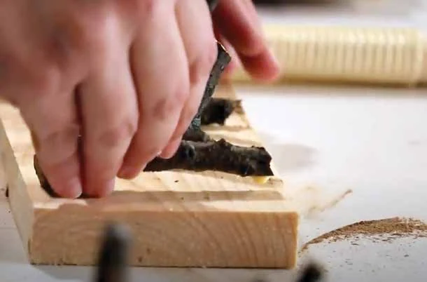 A hand positioning a prepared twig against a wooden base during glue assembly.