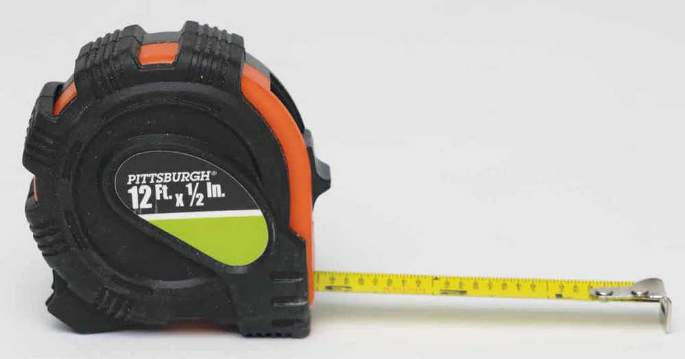 Maplewoodshop photograph of a retractable tape measure with its numbered blade and end hook extended.